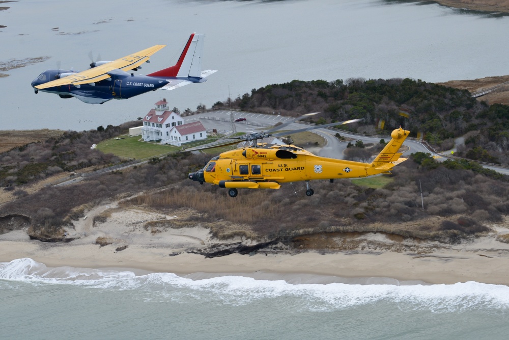 The centennial HC-144 Ocean Sentry airplane and MH-60 Jayhawk helicopter fly over a retired Coast Guard station museum at Coast Guard beach, Eastham, Massachusetts, Monday, Dec. 16, 2019. Coast Guard Air Station Cape Cod will celebrate 104 years of aviation in Mass., and 50 years on Cape Cod. (U.S. Coast Guard photo by Petty Officer 2nd Class Nicole J. Groll)
