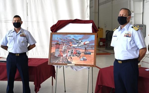 Command Master Chief Jacob Linder and Capt. Scott Langum, commanding officer, Air Station Cape Cod, stand next to a painting to commemorate the 50th anniversary of the air station. The groundbreaking ceremony took place August 29, 1970, and a few weeks later the first aircrafts were transferred from the base in Salem and Rhode Island. (U.S. Coast Guard photo by Petty Officer 2nd Class Amanda Wyrick)